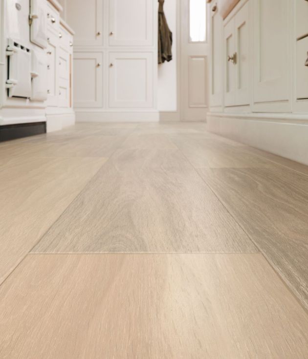 Close up floor-level shot of brown woodgrain LVP floor in kitchen, with white cabinetry, oven door, and entry door in background