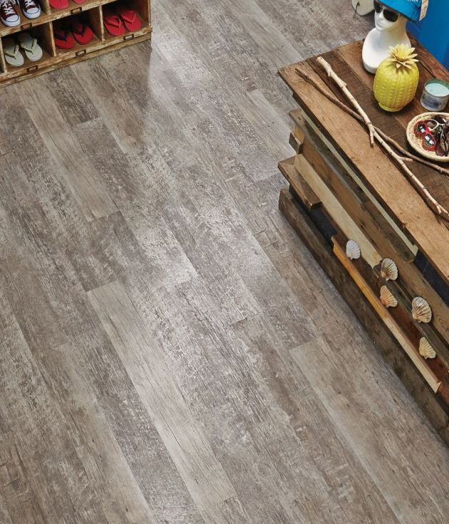Retail space with aged gray woodgrain flooring, weathered counter topped with sunglasses and pineapple, and cubby shelf filled with flipflops and sneakers