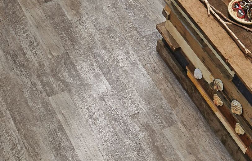 Retail space with aged gray woodgrain flooring, weathered counter topped with sunglasses and pineapple, and cubby shelf filled with flipflops and sneakers