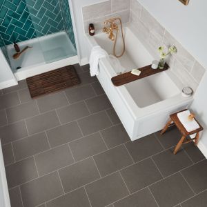 Bathroom scene with teal herringbone shower, floor mat, bathtub, and small table over medium gray concrete-style grouted tile