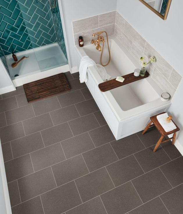 Bathroom scene with teal herringbone shower, floor mat, bathtub, and small table over medium gray concrete-style grouted tile