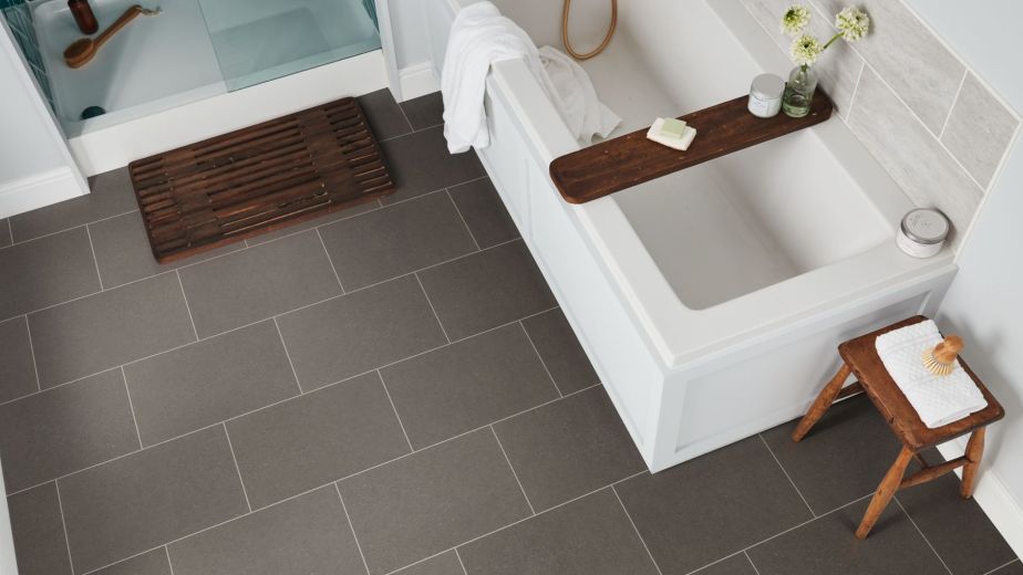 Bathroom scene with teal herringbone shower, floor mat, bathtub, and small table over medium gray concrete-style grouted tile