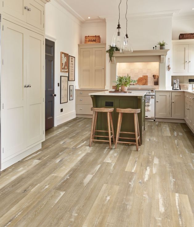 Kitchen with taupe cabinetry, high shade variance taupe woodgrain floor, olive island with stools under pendant lights, with various farmhouse decor