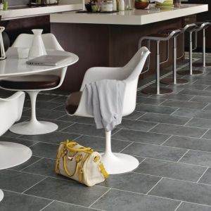 Kitchen with dark cabinetry and island, with white dining table and chairs with purse on gray tile floor