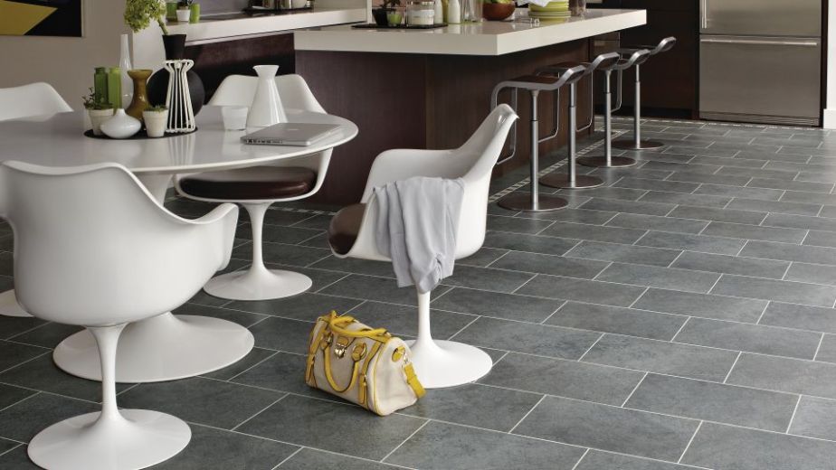 Kitchen with dark cabinetry and island, with white dining table and chairs with purse on gray tile floor