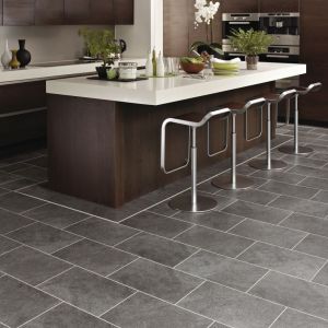 Kitchen with dark cabinets and island with silver barstools over gray tile floor with decorative border