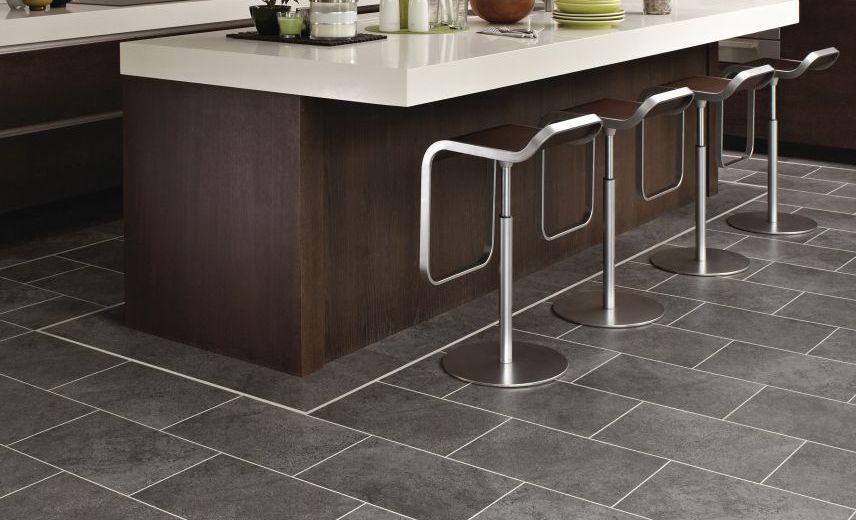 Kitchen with dark cabinets and island with silver barstools over gray tile floor with decorative border