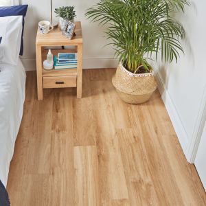 Coastal bedroom with white and blue bedding, wooden nightstand, and potted palm houseplant in room with blond oak LVP floors