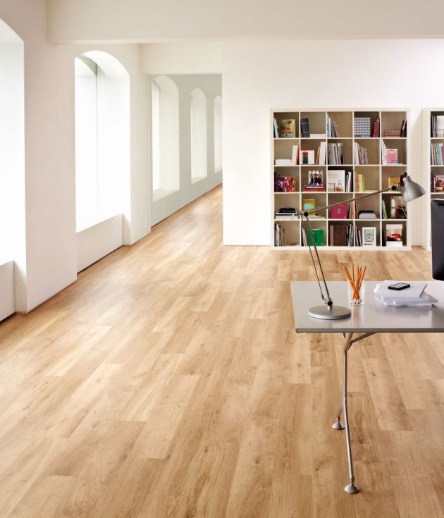 Luxury home office space featuring bank of arced windows, modern computer desk, and cubby shelving packed with books, in large room with white walls and blonde oak flooring