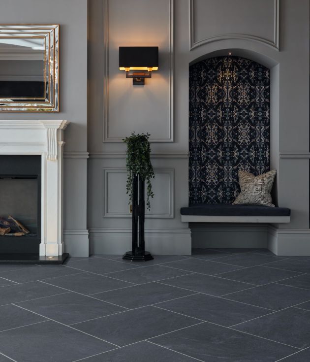 Dark, dramatic living space with white fireplace, gold mirror, sconce, houseplant, and alcove area, with off-white wainscoted walls and rectangular charcoal tiles staggered and grouted