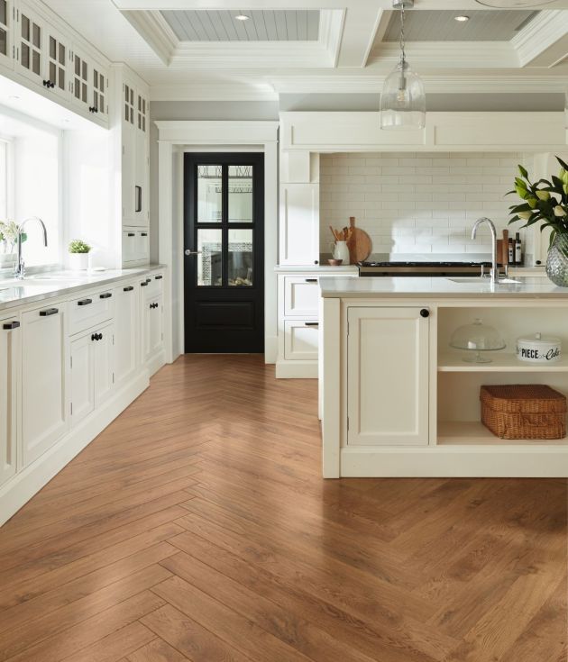 Bright kitchen with white cabinetry, black door, and white island, with silver glass pendant lights, and warm medium brown herringbone woodgrain LVP floor