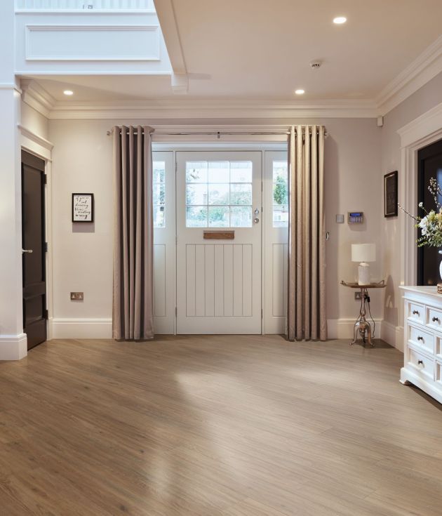 Merino Oak medium brown LVP flooring installed in a diagonal in entryway, with white farmhouse door, curtains, side table, and buffet table