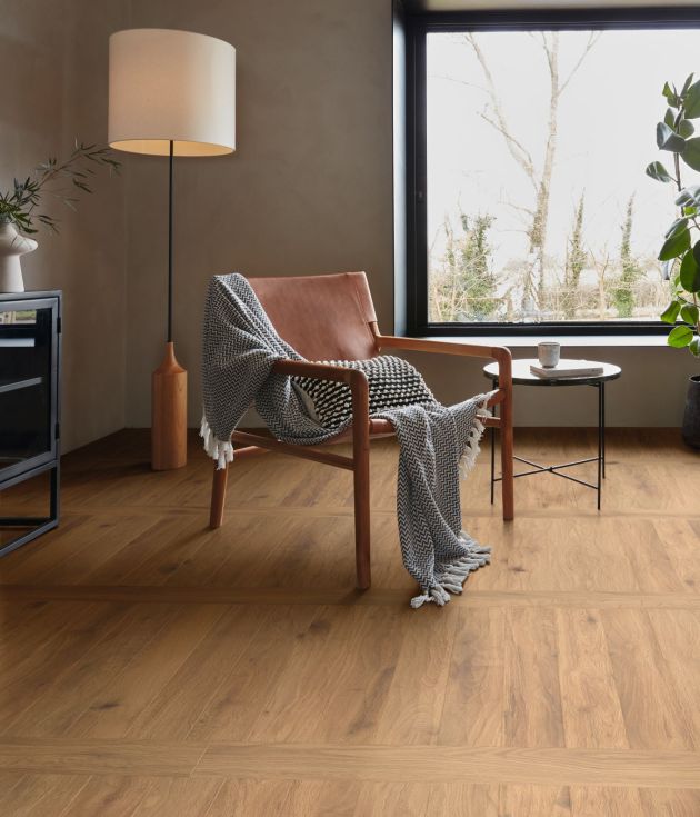 Mid-century chair and floor lamp before large window, with golden brown floor installed with perpendicular planks for a grid effect