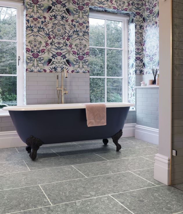 Bathroom scene with clawfoot tub before two large windows, with floral wallpaper and wall tile and gray rectangular terrazzo-look LVT with grout lines