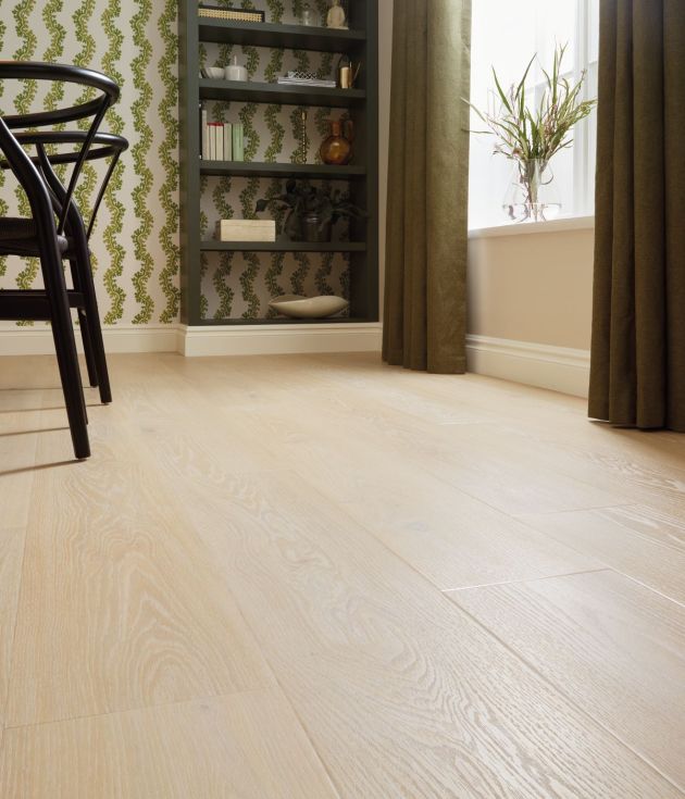 Dining room floor, a pale taupe wood-look floor with black chairs and bookshelf in background, with houseplant on windowsill surrounded by drapes
