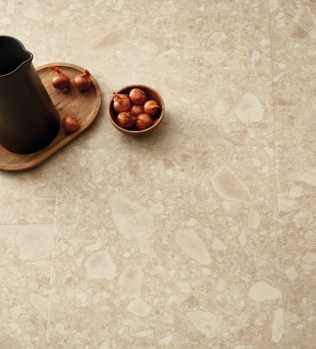 Overhead shot of modern black pitcher atop wooden tray, beside bowl of onions on beige and taupe terrazzo tile