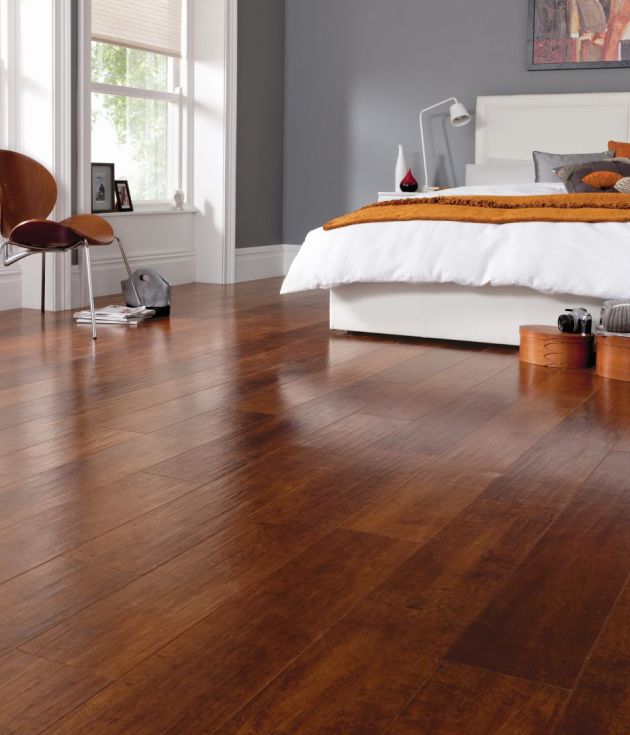 Bedroom with modern artwork hanging behind bed, wooden chair, windows, and wooden bins on reddish brown cherry woodgrain floor with hand-scraped texture