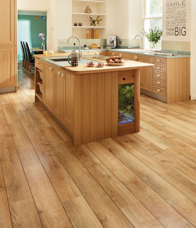 Bright kitchen with warm-toned wood cabinetry, island, and blonde woodgrain floor, with peek of dining area in background