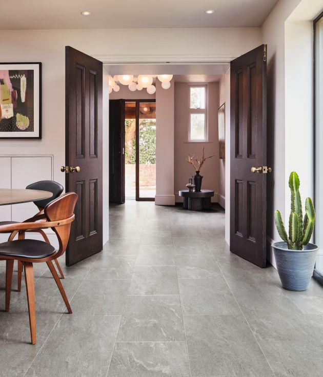 Dining space with artwork, modern chairs, and potted cactus looking beyond wooden doors into entry area with low corner table