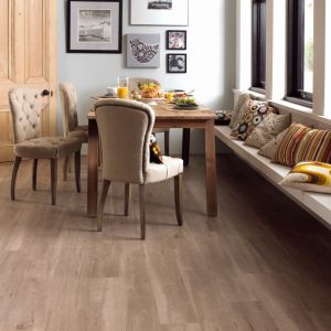 Dining space with table and bench seating along window with artwork on wall beside wooden door, with cool gray-brown woodgrain floor