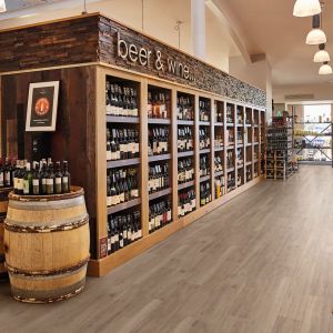 Retail space featuring shelves filled with beer and wine bottles, with wine barrels on end and bins of breads and fruit