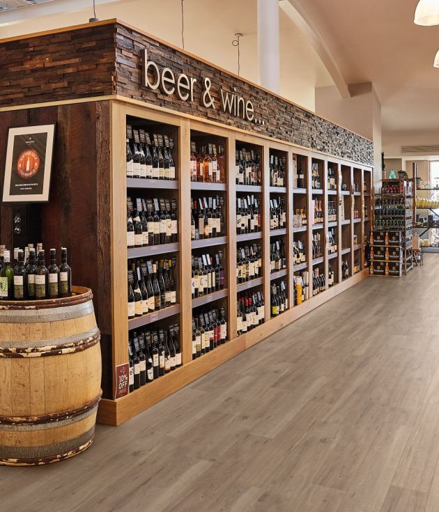 Retail space featuring shelves filled with beer and wine bottles, with wine barrels on end and bins of breads and fruit