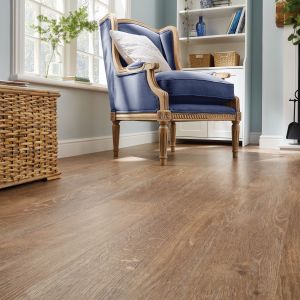 Living space featuring medium golden brown woodgrain floor, woven trunk, window, and blue armchair before built-in shelf and fireplace