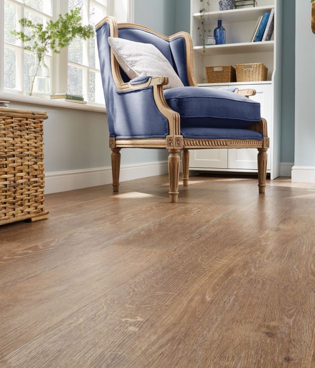 Living space featuring medium golden brown woodgrain floor, woven trunk, window, and blue armchair before built-in shelf and fireplace