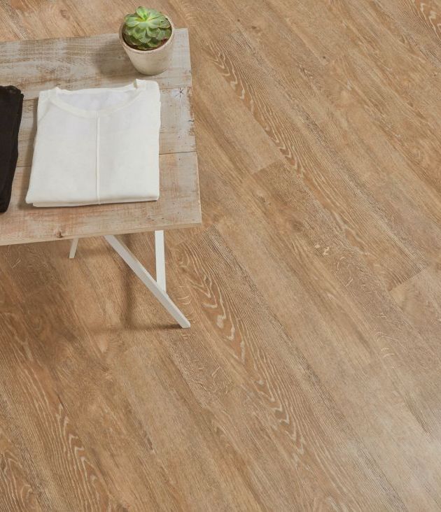 Retail space with table topped with two pairs of shiny silver shoes, two shirts, and a potted succulent in space with diagonally-installed brown reclaimed wood LVP flooring