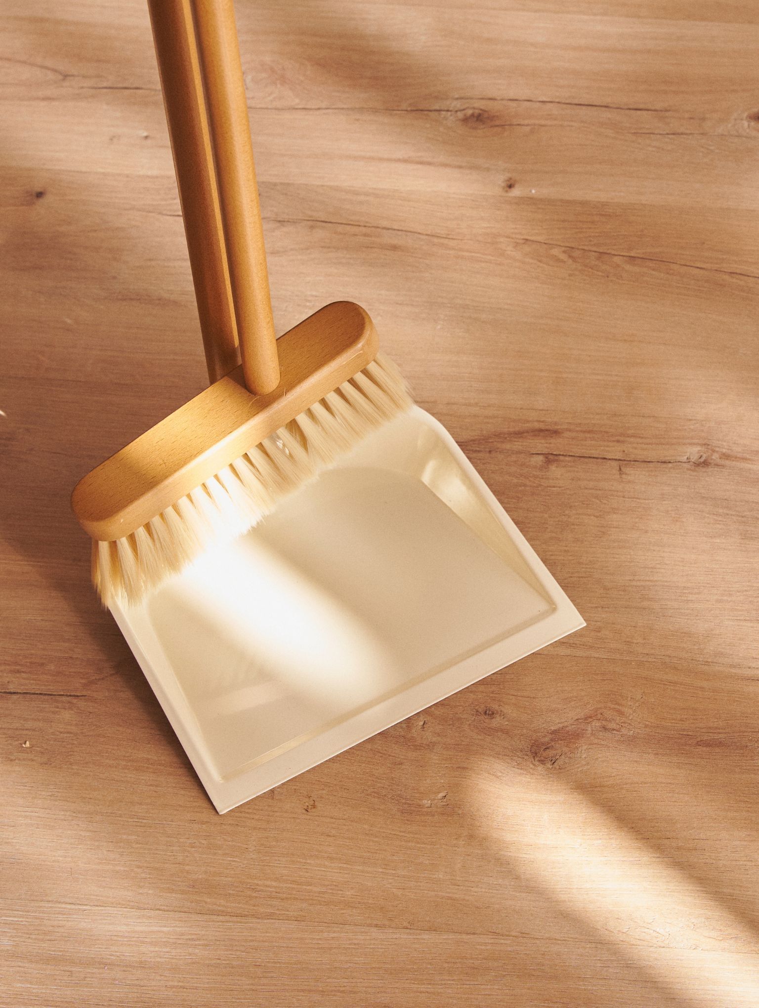 Wooden broom and sweep bucket over hardwood floor with natural light